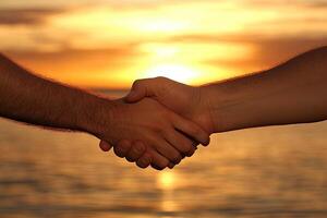 Two hands shaking in agreement at sunset over water photo