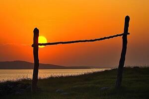 Sunset silhouettes of simple wooden posts and a rustic fence against a vibrant orange sky over a calm body of water photo