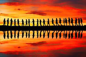 Silhouette of people hand-in-hand at sunset, reflected in water photo