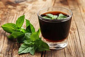 Dark drink with fresh mint leaves on rustic wooden table photo