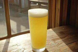 Light, golden-yellow beer in tall glass, frothy top, sunlight through window photo