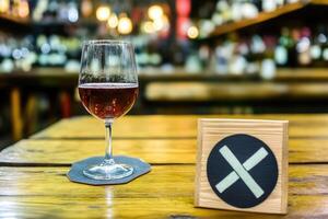 A glass of wine on a wooden table with a social distancing sign photo