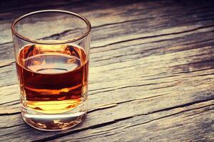 A shot glass of amber liquid on a rustic wooden table photo