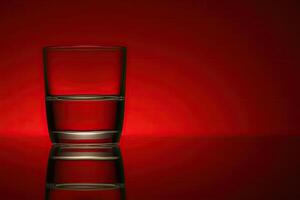 Half-full glass of water against a red backdrop photo
