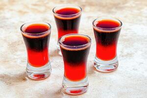Four shot glasses filled with layered red and dark drinks photo