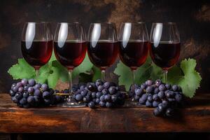 Four glasses of red wine, with grapes and leaves, on a rustic wooden surface photo
