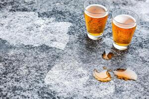 Two glasses of light amber beer on a mottled gray surface with spilled beer photo
