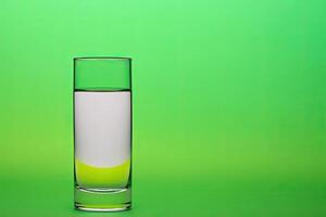 Clear glass tumbler half-filled with clear liquid against a vibrant green backdrop photo