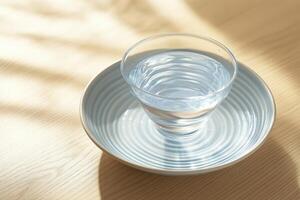 A glass of water on a patterned plate, bathed in sunlight photo