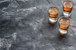 Three small glasses of amber liquid on dark stone photo