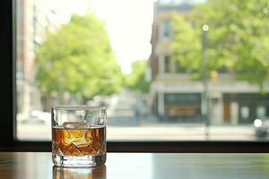 A glass of amber liquid with ice, on a bar, with a city view photo