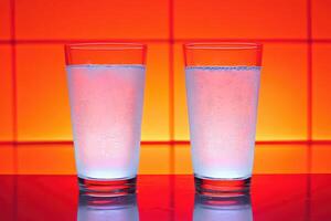 Two glasses of iced water against a vibrant orange background photo