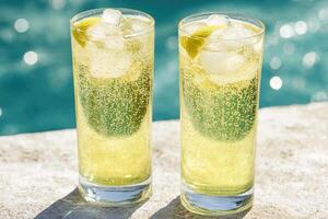 Two chilled, light-yellow drinks on a poolside table photo