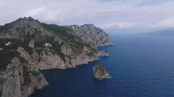 Slow pan of Capri's coastline with cliffs, whitewashed buildings, lush greenery, and clouds partially covering the rugged terrain. video