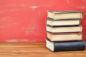 Stack of vintage books on a wooden table against a red background photo