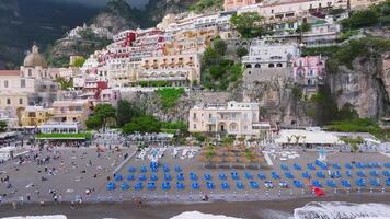 Aerial view of Positano on the Amalfi Coast, showing colorful cliffside buildings, lush greenery, a beach with blue chairs, and gradual motion. video