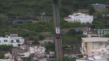 Aerial view of a funicular railway moving through greenery, terraced gardens, and whitewashed buildings on the island of Capri, Italy. video