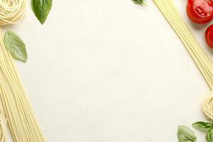 Fresh pasta, tomatoes, and basil arranged on a white surface photo