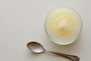 Creamy, light-yellow, textured food in a glass bowl, with a spoon beside it photo