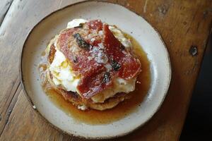 Savory pancake stack with prosciutto, whipped cream, and syrup photo