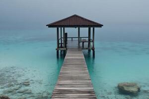 A wooden pier leads to a small hut in the ocean photo