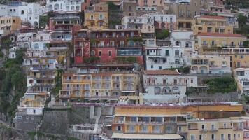 Aerial view of Positano on the Amalfi Coast, showcasing pastel buildings cascading down cliffs, greenery, and overcast skies with slow sweeping motion. video