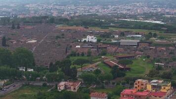 Aerial view of Pompeii's ruins, showcasing streets, walls, and structures. The scene includes greenery, modern borders, and Mount Vesuvius in the distance. video