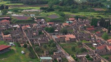 Aerial view of Pompeii's ruins, featuring stone walls, red tiled roofs, streets, greenery, open fields, and distant modern buildings in Italy. video