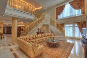 Luxurious, two-story living room with opulent gold accents, a grand staircase, and large windows photo