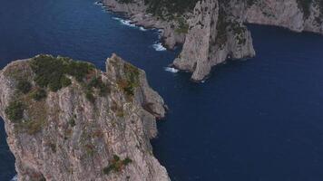 Aerial view of Capri, Italy, showing cliffs, rugged coastlines, hillside buildings, lush greenery, and unique rock formations under an overcast sky. video