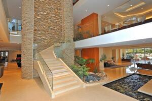 Modern, luxurious foyer with a dramatic stone wall, a curved staircase, and a serene water feature photo