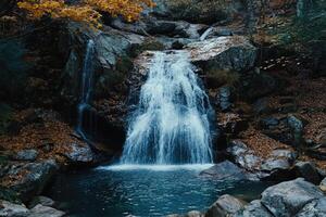 Autumn waterfall cascading over rocks into a tranquil pool, surrounded by fall foliage photo