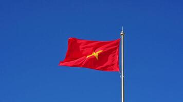 red Vietnamese flag with on a high flagpole flutters in the wind on background of blue sky video