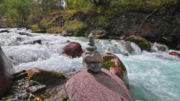 A cairn of small stones against the background of a slowly flowing mountain river. A stream flowing through the rocks. video