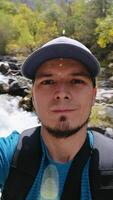 A selfie of a Caucasian male tourist against the background of a fast-flowing mountain river. video