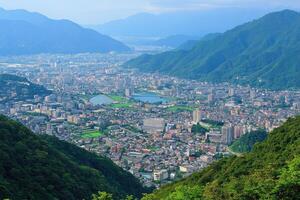 City nestled in valley, surrounded by mountains. Lush greenery, urban sprawl, tranquil lake photo