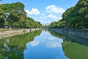 Canal lined with lush trees, reflecting a clear blue sky photo