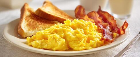 The delicious breakfast featuring scrambled eggs, crispy bacon, and toasted bread. photo