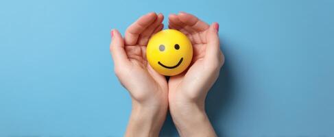 The cheerful yellow smiley ball cradled in caring hands against a blue background. photo