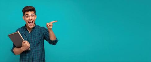 The enthusiastic man pointing while holding a notebook on a vibrant blue background. photo