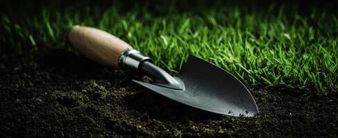 The trowel resting on dark soil surrounded by vibrant green grass. photo
