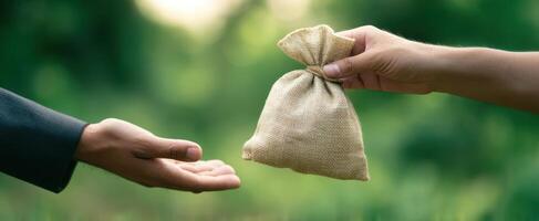 The hands exchanging a burlap bag representing a financial transaction outdoors. photo