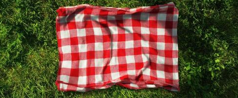 The red checkered picnic blanket on a lush green lawn. photo