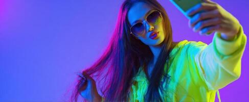 The vibrant woman taking a stylish selfie with neon lights. photo