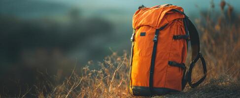 The vibrant orange backpack resting on a grassy hillside in nature. photo