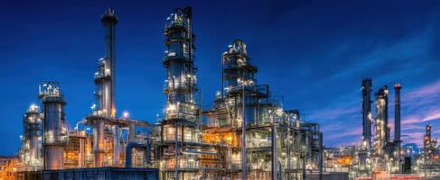 The impressive industrial refinery illuminated at dusk with vibrant city skyline. photo