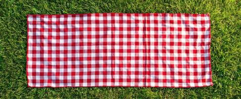The vibrant red and white checkered picnic blanket on lush grass. photo