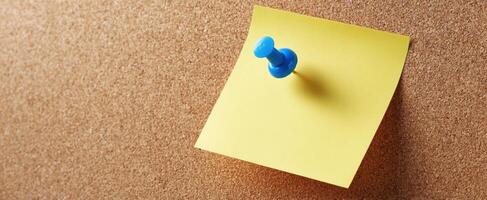 The blue pushpin holding a yellow note on a corkboard background. photo
