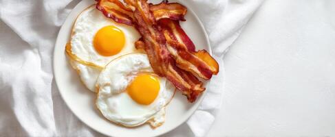 The delicious breakfast of fried eggs and crispy bacon on a white plate. photo