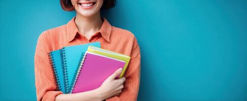 The cheerful woman holding colorful notebooks against a vibrant blue background. photo